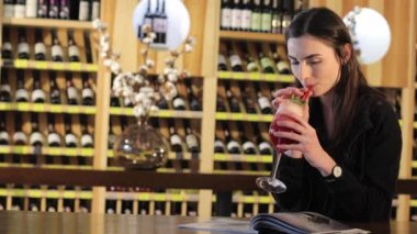 Genç bir kız bir moda Restoran, kırmızı egzotik kokteyl içme kadın tabloda bir kokteyl içer