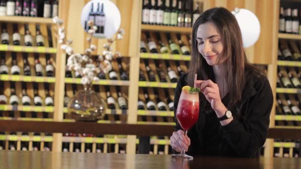 Een jong meisje drinkt een cocktail op een tafel in een restaurant mode, een jong meisje met een rode exotische cocktail aan een tafel in een restaurant of bar, vrouw rode exotische cocktail drinken — Stockvideo