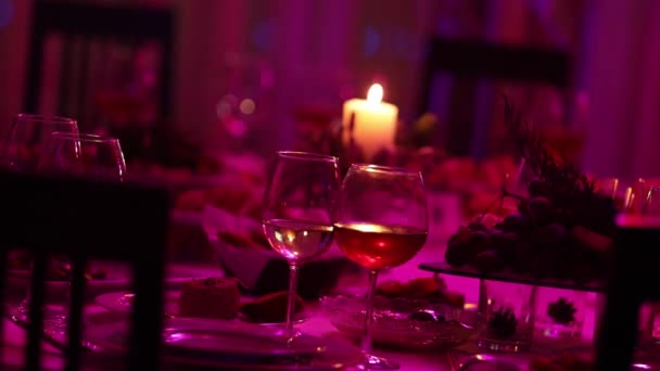 Feestzaal tafel in een restaurant met bril en een kaars, een glas met rode en witte wijn op een feestzaal tafel op een achtergrond van een brandende kaars, een decoratieve wax kaars in de hanger aan een tabel — Stockvideo