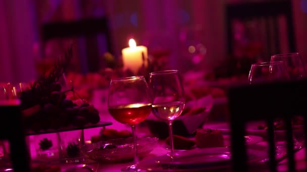 Банкетный стол в ресторане с бокалами и свечой, бокал с красным и белым вином на банкетном столе на фоне горящей свечи, декоративная восковая свеча в кулоне на столе — стоковое видео