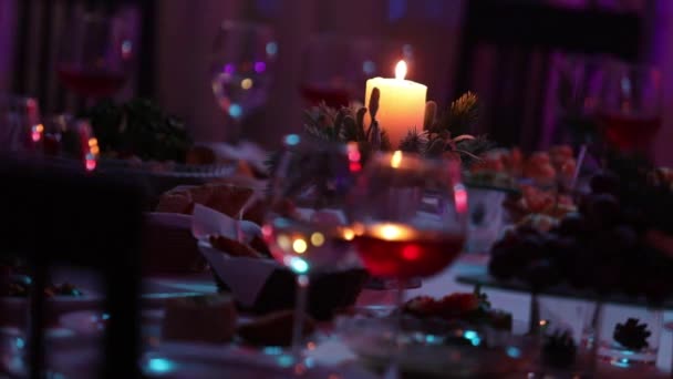 Slavnostní stůl v restauraci s brýlemi a svíčka, sklenice červené a bílé víno na banket stůl na pozadí hořící svíčkou, dekorativní voskovou svíčku v přívěsku na stůl — Stock video