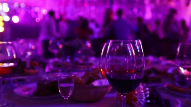 Een partij van de jeugd in een restaurant of een discotheek, feestzaal tabellen met alcohol en voedsel tegen de achtergrond van de silhouetten van dansende mensen, fase licht en paarse opvulling, ondiepe scherptediepte — Stockvideo
