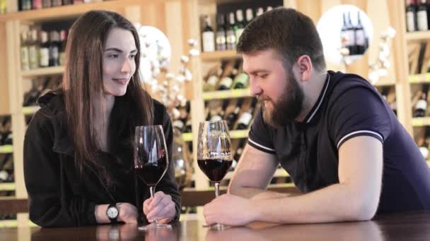 Uma menina e um cara em um restaurante se comunicam e bebem vinho tinto, um jovem casal bebe vinho tinto em uma mesa em um restaurante ou café. — Vídeo de Stock