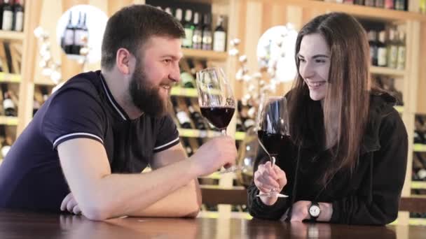 Una chica y un chico en un restaurante se comunican y beben vino tinto, una pareja joven bebe vino tinto en una mesa en un restaurante o cafetería — Vídeo de stock