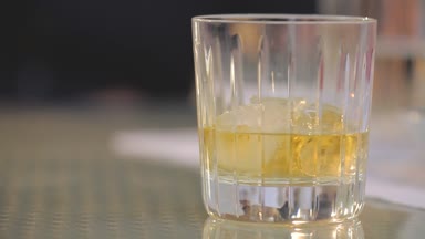 Adam bir bardak viski buz tablosundan alır, bir bardak buzlu viski koyar tablo, yakın çekim, sığ derinlik-in tarla, ahşap masa üzerinde businessmans elinde viski bardak