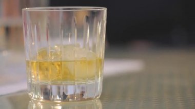 Adam bir bardak viski buz tablosundan alır, bir bardak buzlu viski koyar tablo, yakın çekim, sığ derinlik-in tarla, ahşap masa üzerinde businessmans elinde viski bardak