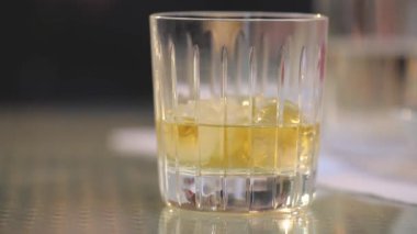 Adam bir bardak viski buz tablosundan alır, bir bardak buzlu viski koyar tablo, yakın çekim, sığ derinlik-in tarla, ahşap masa üzerinde businessmans elinde viski bardak