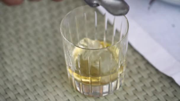 Il cameriere mette cubetti di ghiaccio in un bicchiere con whisky, un bicchiere di whisky sul tavolo, un bicchiere di whisky laici cubetti di ghiaccio, un bicchiere di whisky con ghiaccio sul tavolo — Video Stock