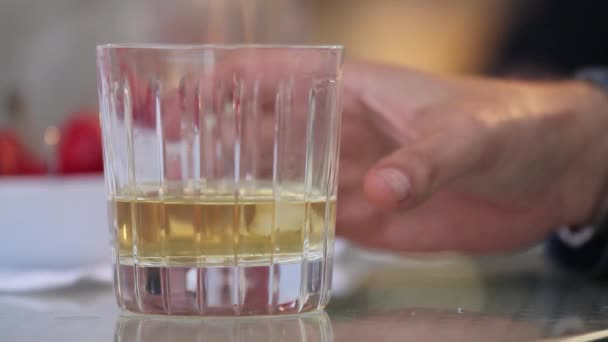 Мужчина берет стакан виски со льдом со стола, кладет стакан виски со льдом на стол, крупным планом, мелкой глубиной поля, стаканы виски в руках бизнесменов на деревянный стол — стоковое видео