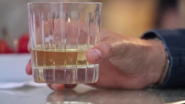 De man neemt een glas whiskey met ijs uit de tabel, zet een glas whiskey met ijs op de tafel, close-up, ondiepe scherptediepte, glazen whisky in handen van de businessmans op houten tafel — Stockvideo