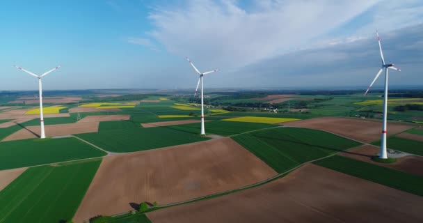 Vol au-dessus des champs agricoles verts aux éoliennes se tenant au loin — Video