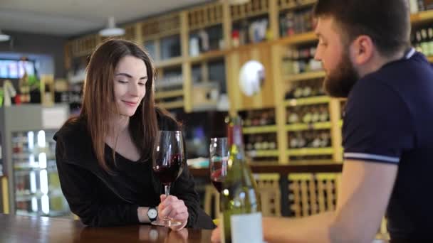 Een man en een vrouw zijn het drinken van rode wijn in glazen, het interieur van een restaurant, een jonge man en een meisje zijn het drinken van wijn op een tafel in een restaurant, tegen een achtergrond van een wijn plank, een mannetje hipper — Stockvideo