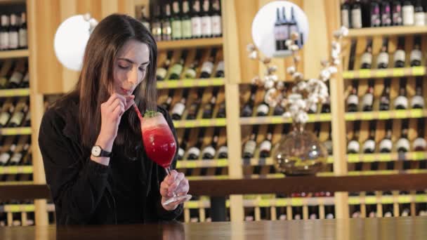 Uma menina bebe um coquetel vermelho no bar no bar, mulher bebendo coquetel exótico vermelho — Vídeo de Stock