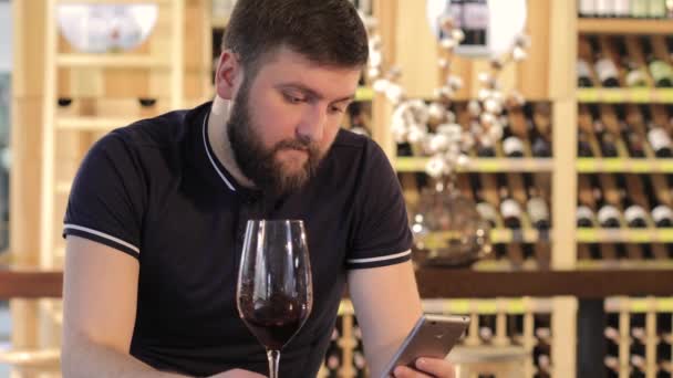 Mladý muž pomocí smartphone, zatímco pití červeného vína, osamělý muž se sklenkou červeného vína, mladý muž v restauraci u sklenky červeného vína, člověk pije červené víno u stolu v restauraci — Stock video