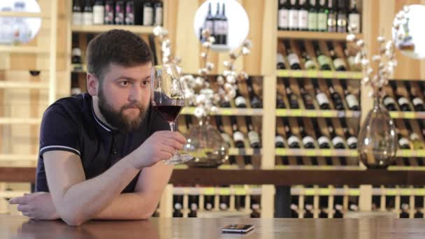 Un giovane che usa uno smartphone mentre beve un vino rosso, un uomo solo con un bicchiere di vino rosso, un giovane in un ristorante con un bicchiere di vino rosso, un uomo che beve vino rosso a un tavolo in un ristorante — Video Stock