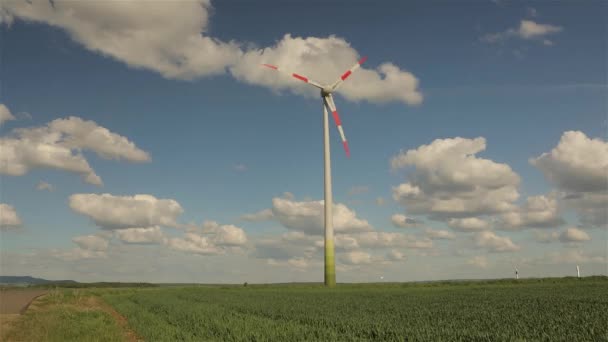 Wind generator against the background of clouds floating in the sky. Rotation of the large wind generator blades. Panoramic view of the agricultural landscape. Sunny day. Europe. Timelapse — Stock Video