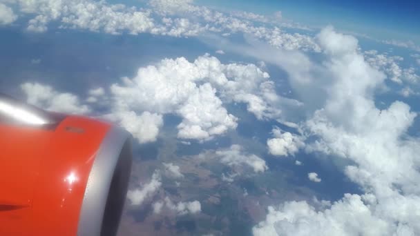 Nézd a repülőgép ablakból a kék ég és fehér felhők, egy narancs turbina a szárnya a gépet, a nézetet a föld az égen, a felhőkön át, a fehér felhők lebegnek a föld felett — Stock videók