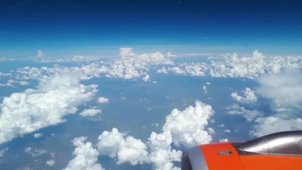 Pohled z okna letadla na modrou oblohu a bílé mraky, oranžové turbína na křídle letadla, pohled na zemi z nebe, mraky, plovoucí na bílé mraky nad zemí — Stock video