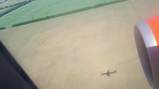 Η σκιά του πετούν αεροπλάνο στο έδαφος σε μια ηλιόλουστη ημέρα. Θέα από το παράθυρο του αεροπλάνου. Σκιά του πλατάνου. Πετώντας πάνω από το πεδίο και το δάσος κατά την προσγείωση στο αεροδρόμιο — Αρχείο Βίντεο