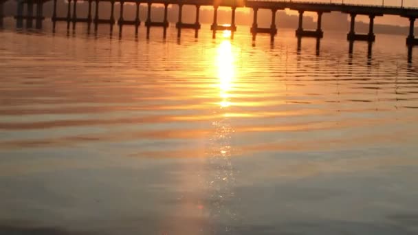 El sol sale sobre el río después del puente, reflejos de agua — Vídeo de stock