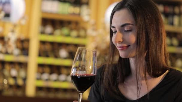 Mulher tomando um copo de vinho tinto, Uma menina com um copo de vinho tinto, uma jovem menina bonita está bebendo vinho tinto em um restaurante — Vídeo de Stock