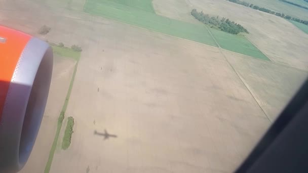 晴れた日に地面に飛行の機体の影。飛行機の窓からの眺め。平面の影。フィールドと空港に着陸中の森上空 — ストック動画