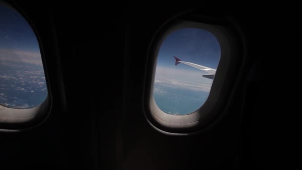 Blick auf blauen Himmel und Wolken durch das Flugzeugfenster, Nahaufnahme Flugzeugfenster mit Flugzeugflügel, Reisekonzept — Stockvideo