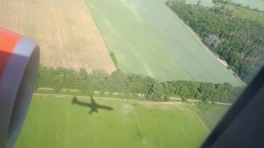 Gölge güneşli bir yerde uçan bir uçağın. Uçak penceresinden görüntüleyin. Uçak gölgesi. Alan ve orman süre havaalanına iniş üzerinde uçan