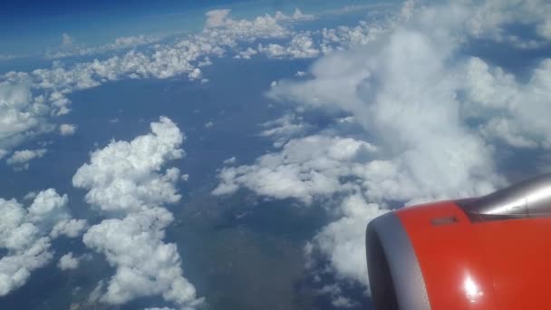 Pohled z okna letadla na modrou oblohu a bílé mraky, oranžové turbína na křídle letadla, pohled na zemi z nebe, mraky, plovoucí na bílé mraky nad zemí — Stock video
