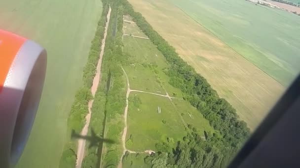 Cień latający samolot na ziemi w słoneczny dzień. Widok z okna samolotu. Cień samolotu. Latające nad pola i lasu podczas lądowania na lotnisku — Wideo stockowe