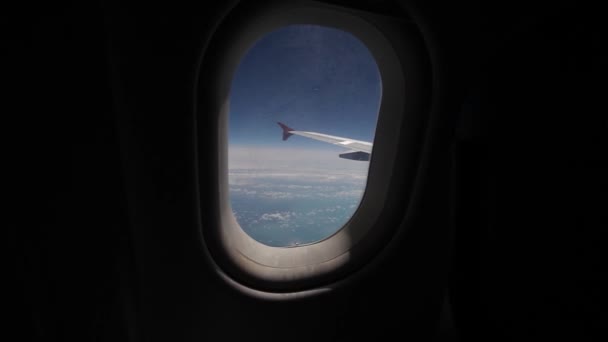 Blick auf blauen Himmel und Wolken durch das Flugzeugfenster, Nahaufnahme Flugzeugfenster mit Flugzeugflügel, Reisekonzept — Stockvideo