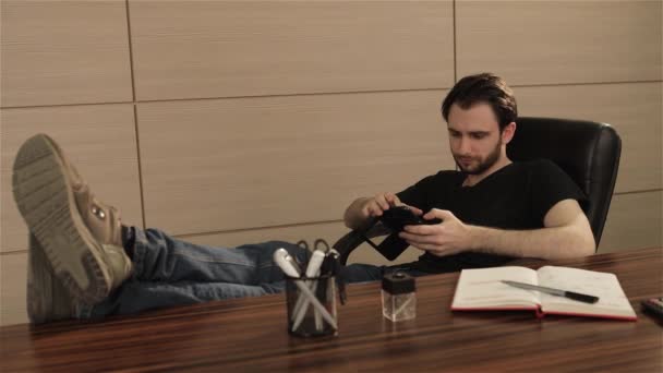 El hombre de negocios en la oficina juega un juego en su teléfono móvil. Las emociones brillantes en las personas se enfrentan. Joven trabajando desde la oficina usando un teléfono inteligente — Vídeo de stock