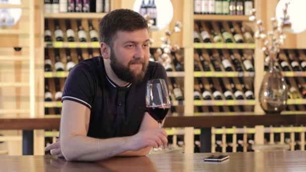 Ένας μοναχικός άνθρωπος με ένα ποτήρι κόκκινο κρασί, νεαρός άνδρας σε ένα εστιατόριο με ένα ποτήρι κόκκινο κρασί, ένας άνθρωπος πίνει κόκκινο κρασί σε ένα τραπέζι σε ένα εστιατόριο — Αρχείο Βίντεο