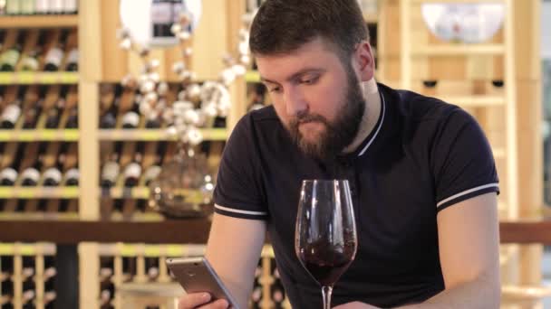Молодой человек, использующий смартфон во время питья красного вина, одинокий человек с бокалом красного вина, молодой человек в ресторане с бокалом красного вина, мужчина пьет красное вино за столом в ресторане — стоковое видео