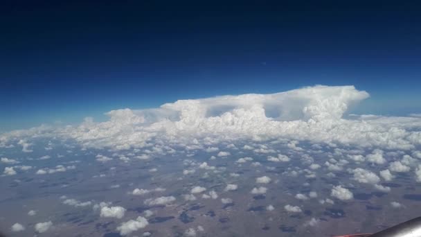 Vista desde la ventana del avión al cielo azul y nubes blancas en un día soleado, un montón de nubes blancas flotan sobre la tierra, una vista de la tierra a través de nubes blancas esponjosas — Vídeo de stock