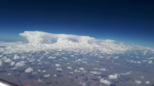 Vista desde la ventana del avión al cielo azul y nubes blancas en un día soleado, un montón de nubes blancas flotan sobre la tierra, una vista de la tierra a través de nubes blancas esponjosas — Vídeo de stock
