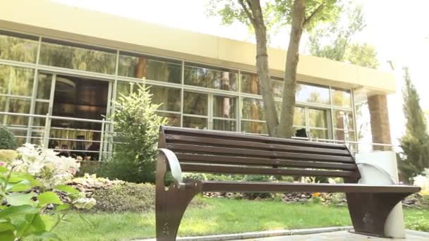 Ένας πάγκος μπροστά από ένα εστιατόριο στο πάρκο, ένα σύγχρονο κτίριο — Αρχείο Βίντεο