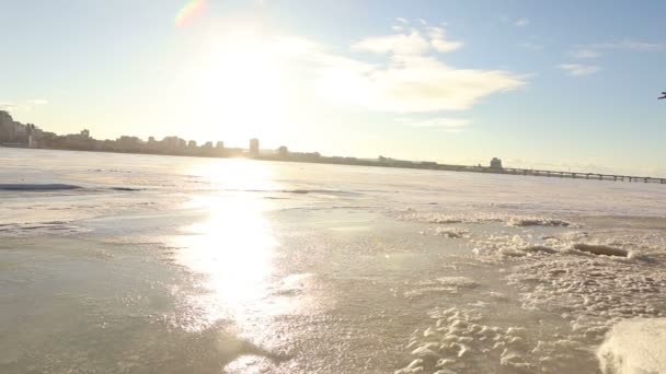 Panorama de la ciudad cerca del río en invierno, una ciudad con edificios altos cerca del río. El río congelado cerca de la gran ciudad una metrópoli de invierno — Vídeos de Stock