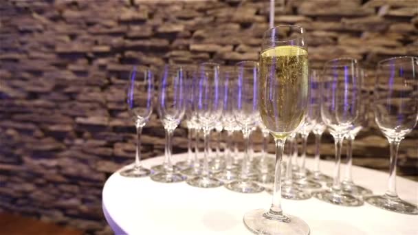 Келих шампанського на фоні порожніх келихів, на столі з шведським столом, піна шампанського в келиху, рух камери, келих шампанського на передньому плані, шампанське в келихах — стокове відео