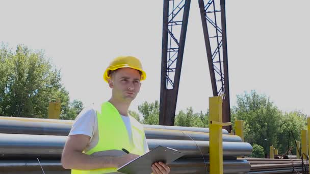 Een man in een fabriek schrijft informatie in een notitieboekje. Jonge mannen in het magazijn, arbeiders in de fabriek inventariseren — Stockvideo