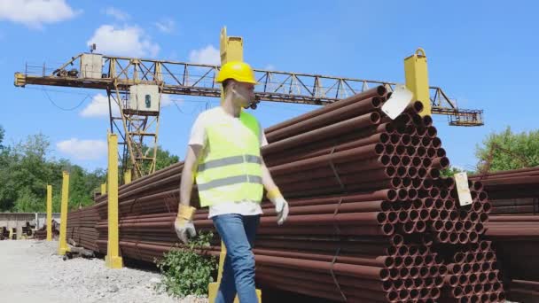 El trabajador del almacén en un chaleco y casco de color amarillo brillante hace un inventario del metal. El gerente cuenta el número de productos — Vídeos de Stock