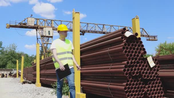 L'ouvrier de l'entrepôt, vêtu d'un gilet et d'un casque jaune vif, fait un inventaire du métal. Le gestionnaire compte le nombre de produits — Video