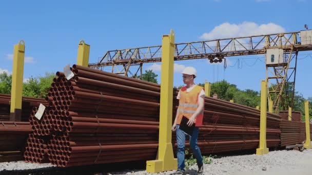 Un trabajador de almacén en un chaleco naranja toma notas en papel. El trabajador del almacén hace un inventario del metal. El gerente cuenta el número de productos — Vídeos de Stock