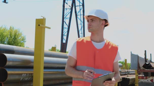 Een magazijnmedewerker maakt aantekeningen op papier. Werknemer in uniform in metalen depot, man met notitieboekje in fabriek. — Stockvideo