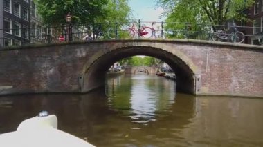 Amsterdam 'da bir köprünün altından geçen turist teknesi. Nehrin üzerindeki köprü, Amsterdam. Amsetrdam 'da insanlar sokaklarda yürüyor