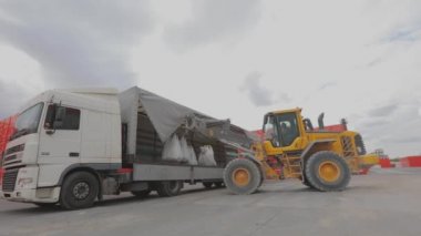 Bir buldozer çantaları bir kamyona boşaltır. Malları kamyondan boşaltıyorum. Buldozer arabadan mal indirir.
