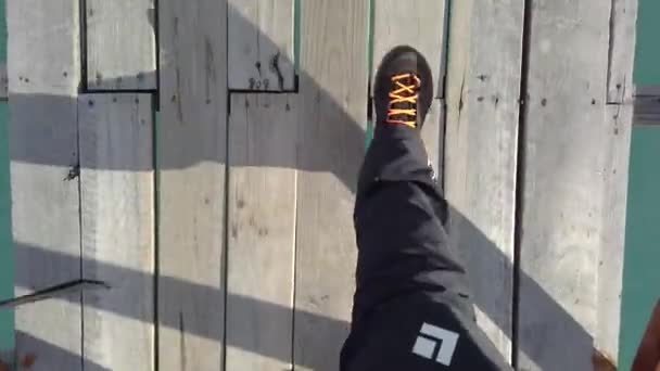 Чоловік ходить по дерев'яному мосту через річку, крупним планом ноги ходять по дерев'яному мосту — стокове відео
