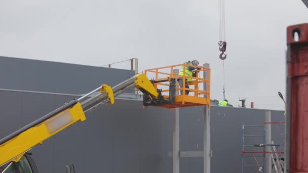 En man på en hiss svetsar ihop en metallkonstruktion. Arbetsflöde på en byggarbetsplats. Metallkonstruktionssvetsning — Stockvideo