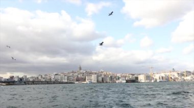 Galata Kulesi, ön planda turistler ve martılarla dolu eğlence tekneleri. Galata Kulesi 'nin arka planında tekneler, rüzgarlı hava