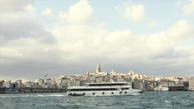 Galata Kulesi, ön planda turistler ve martılarla dolu eğlence tekneleri. Galata Kulesi 'nin arka planında tekneler, rüzgarlı hava